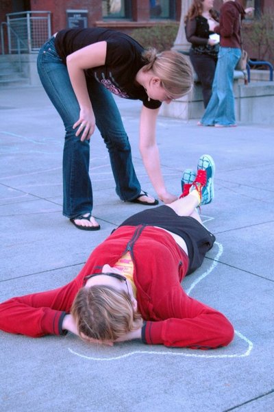 UW Tacoma art student drawing chalk outline of passer-by on campus sidewalk