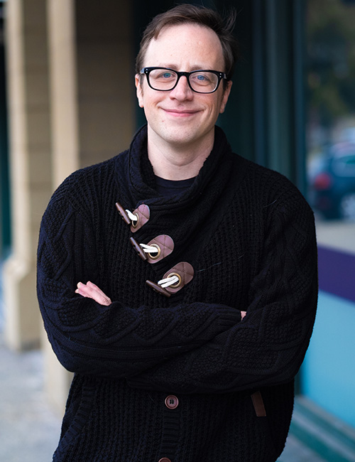 Headshot of alumnus Peter Jung. He is standing with his arms across is stomach. Peter is wearing a dark colored sweater. He has glasses and short, brown hair.