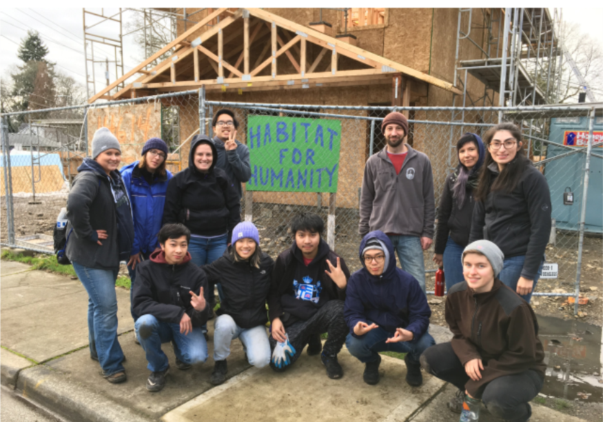A group of UWT volunteers in front of a Habitat for Humanity sign and the house they worked on as their service project.