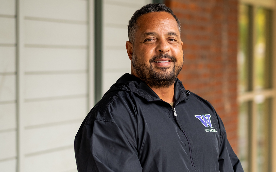 UW Tacoma Educational Administration Program Director Kurt Hatch stands in front of a red brick building. He is wearing a black University of Washington rain jacket.