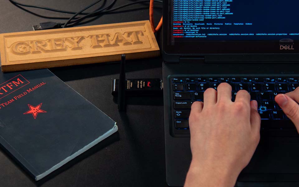 Student coding on computer, with "Grey Hat" placard on desk