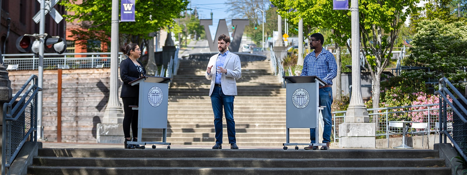 UW Tacoma debate team and mentor on Grand Staircase. Two students standing at portable lecterns, with Dr. Benjamin Meiches at center.