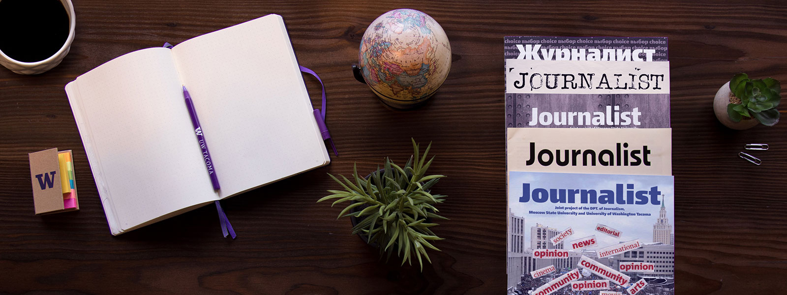 Stack of Journalist magazines with open notebook, globe, coffee cup and plants.