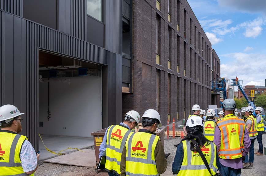 People in yellow construction vests and white hard hats gather for a tour of UW Tacoma's under-construction Milgard Hall.