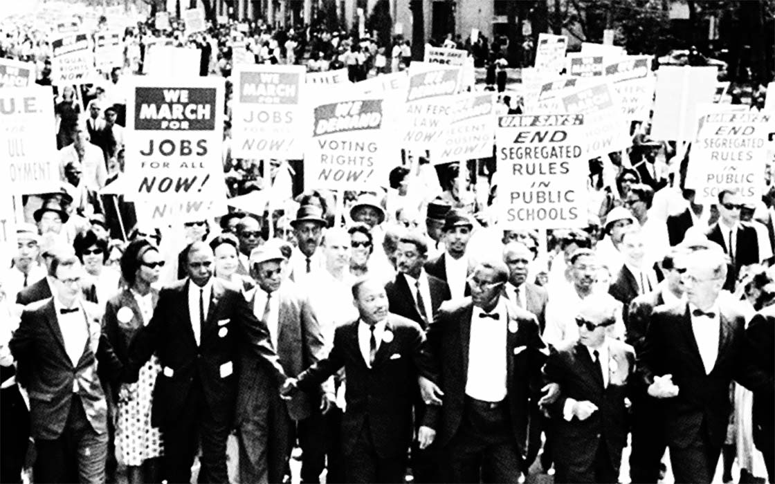 Black-and-white archival photo of Rev. Dr. Martin Luther King Jr. leading a protest march.