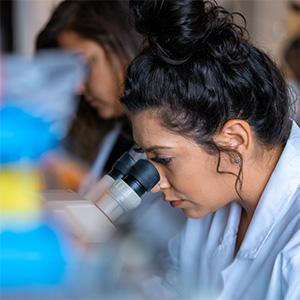 UW Tacoma student in a lab looking into microscope eyepiece