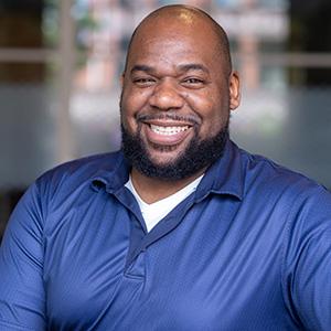 Headshot of UW Tacoma alumnus Michael Jordan. Jordan is smiling and is wearing a purple shirt.