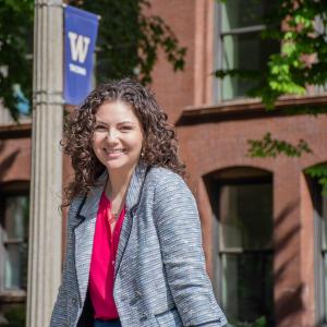 Madilyn Pawlowski poses on top of the UWT flagstone on campus in front of the grand staircase and UWT banner