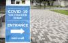 Blue and white sign standing on white and grey pavers, announcing COVID-19 vaccination clinic sponsored by MultiCare