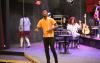 A man stands on the stage at the Tacoma Little Theatre. He has short black hair and is wearing a gold colored shirt.