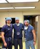 UW Tacoma student Lucas Bjorkheim (right) stands next to two other men in medical scrubs. All of the men are wearing blue medical scrubs and have masks hanging from their necks. They appear to be in a hospital waiting room.